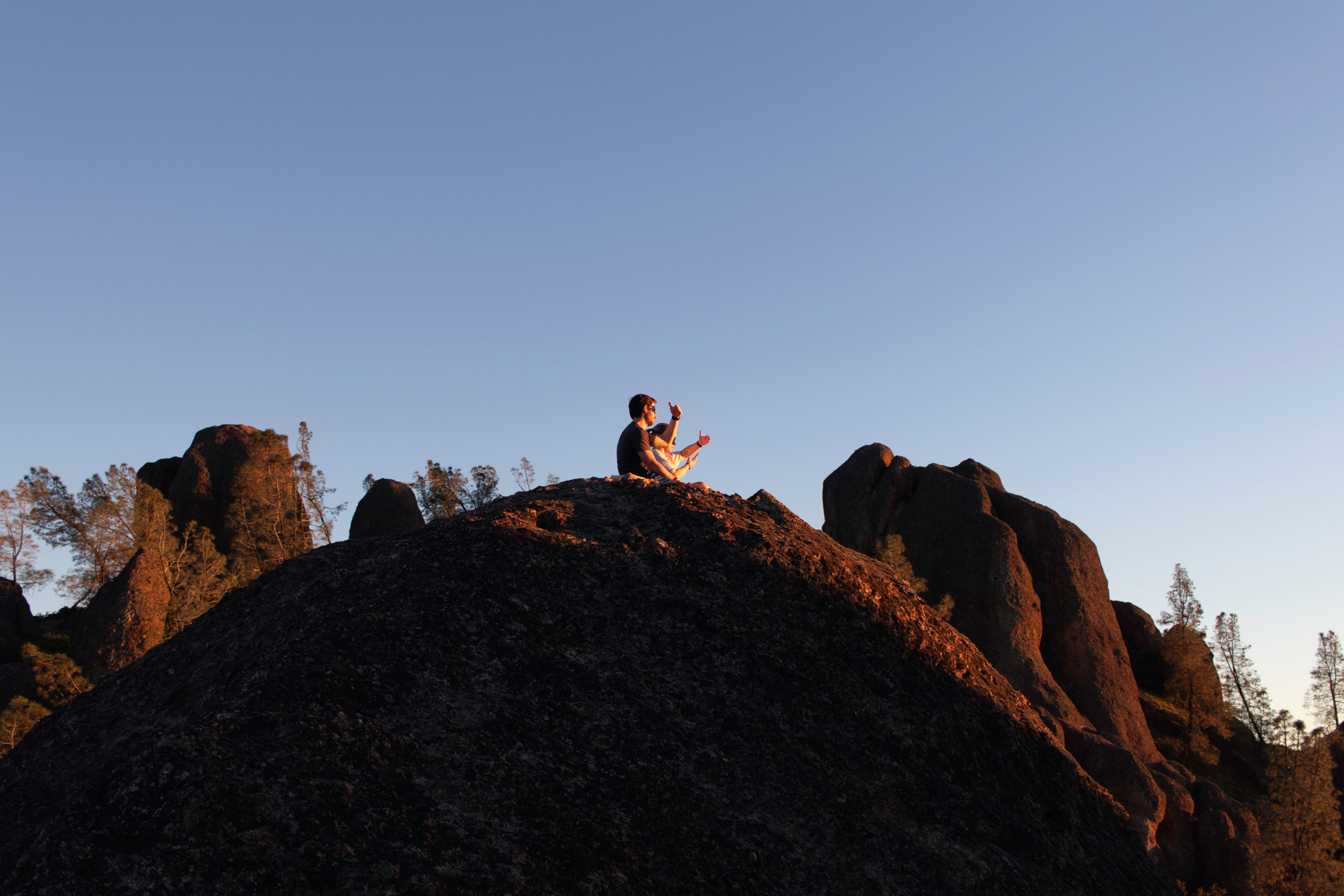 2 hikers sitting on top of rocks looking at the sunset